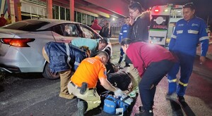 Paramédicos de la Cruz Verde atendiendo sobre la calle al joven motociclista tras el choque con personas alrededor y una ambulancia en el fondo