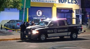 Patrulla de la Policía de Guadalajara con oficiales apoyados en ella frente a una tienda de mofles y el área acordonada donde un hombre murió