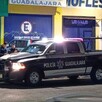 Patrulla de la Policía de Guadalajara con oficiales apoyados en ella frente a una tienda de mofles y el área acordonada donde un hombre murió