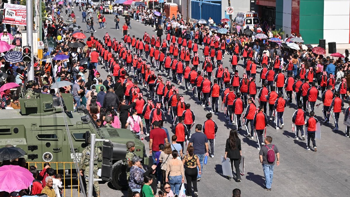 Niños con el uniforme de la escuela desfilan sobre la avenida Madero de Gómez Palacio, un vehículo militar se encuentra dando vuelta detrás de ellos.