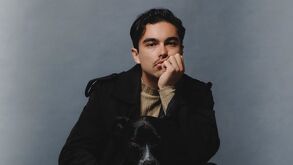 Sergio Mayer Mori en un fondo azul, vestido completamente de negro junto a su perrita, quien es de color negro y se pierde en la foto