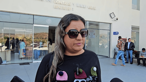 Una mujer (madre de Lalito) con lentes de sol grandes y una camiseta negra con gorros de lana bordados. Está afuera de una oficina de distrito judicial