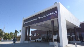 Se observa la fachada del Aeropuerto Internacional de Saltillo, un edificio blanco con gris y un hombre a un lado.