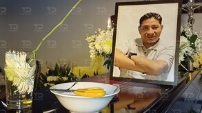 Un ataúd con un plato y un vaso de agua bendita encima, además de una fotografía de la persona fallecida.|