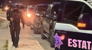 Oficial de la Policía del Estado de Jalisco caminando de noche a un lado de patrullas de la Policía Estatal estacionadas en la calle