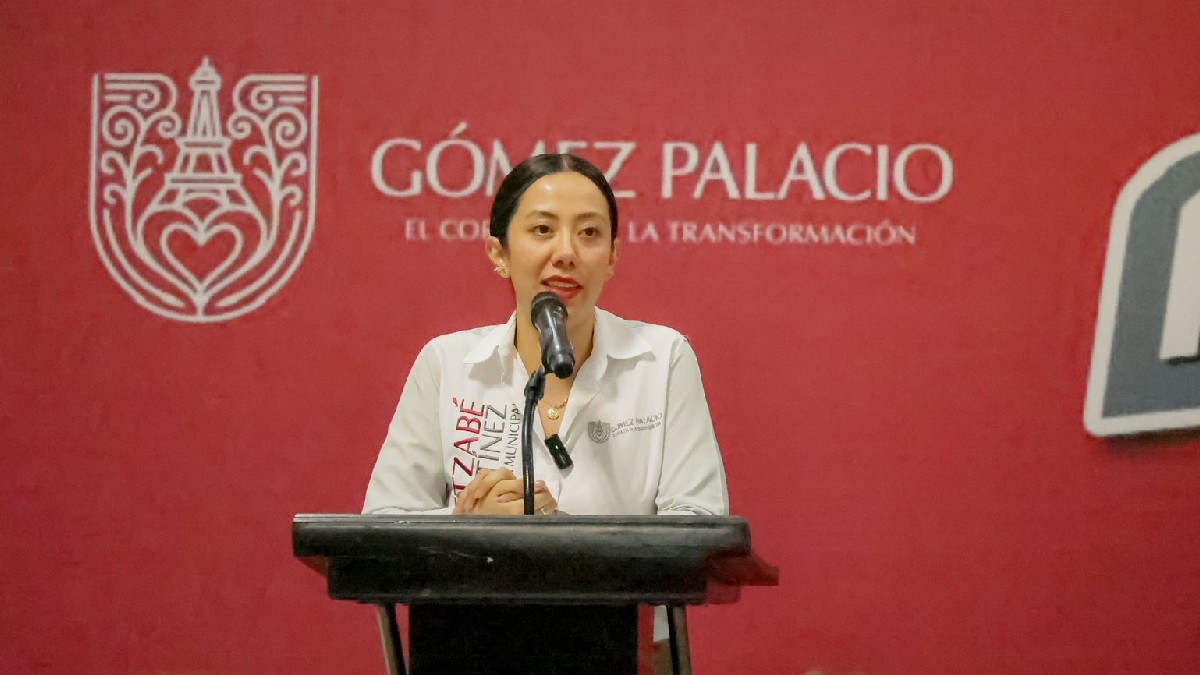 Betzabé Martínez en el estrado hablando en el micrófono en la presentación de Unidad Especializada Anticorrupción. Fondo rojo con el escudo de Gómez Palacio.