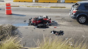 Una motocicleta roja destrozada yace en medio de una autopista, rodeada de escombros y cinta policial. Un coche oscuro con la ventanilla trasera rota