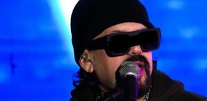Cruz Martínez con lentes oscuros hablando a un micrófono en uno de sus conciertos.