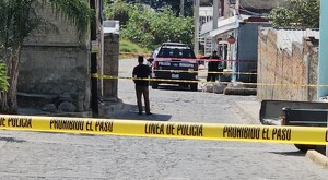 Patrulla y oficiales de la Policía Municipal de Zapopan al exterior de la casa donde ocurrió el asesinato con una cinta policiaca acordonando el área