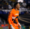 El portero Keylor Navas (Pumas) en un uniforme naranja brillante y guantes blancos grita de emoción en el campo. Está en un partido nocturno frente a las gradas