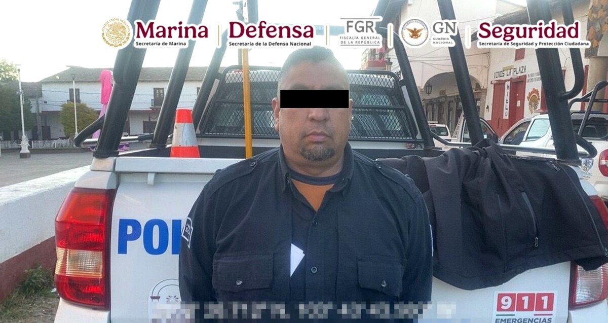 Policía municipal detenido en Jalisco viendo de frente con los ojos censurados vistiendo su uniforme frente a una patrulla