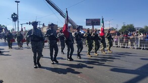 En la imagen se ven a soldados desfilar y personas los observan.