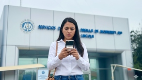 Mujer regia frente a las oficinas de AyD Monterrey, revisando los requisitos para el cambio de titular en su celular