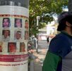 Un hombre de gorra y barba junto a un poste que tiene pegadas las fotografías de personas desaparecidas en Veracruz.