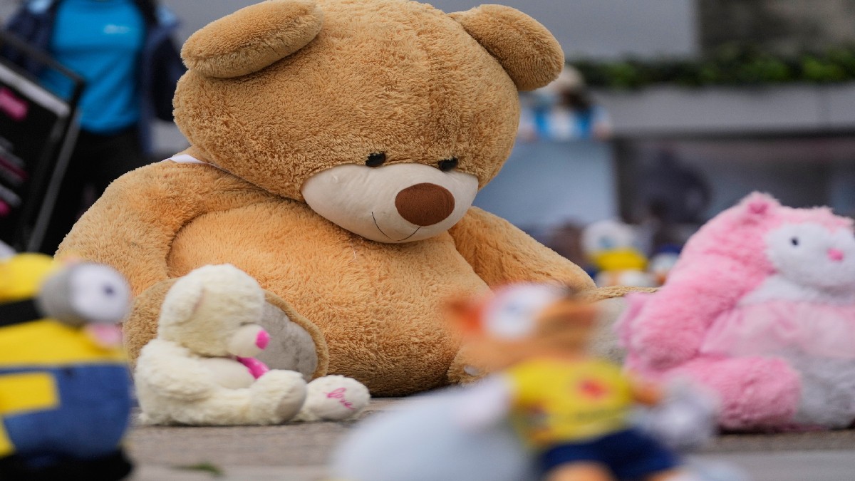 Oso de peluche de gran tamaño en color café al lado de peluche rosa y blanco