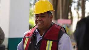 Hombre sonriendo que viste un chaleco y casco amarillo de seguridad.