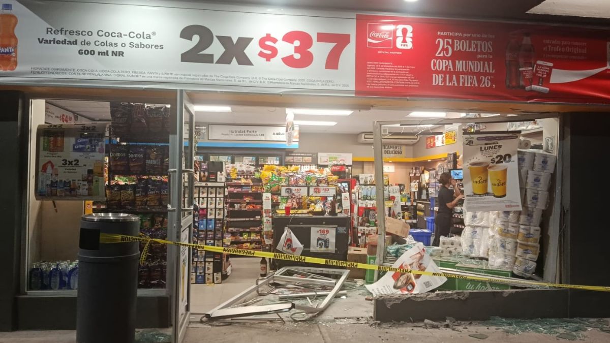 Fotografía tomada por reportero en donde se observa la tienda OXXO completamente destrozada tras ser chocada por automóvil rojo.