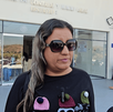 Una mujer (madre de Lalito) con lentes de sol grandes y una camiseta negra con gorros de lana bordados. Está afuera de una oficina de distrito judicial