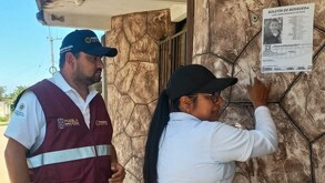 Un hombre y una mujer pegan un boletín de búsqueda para localizar a un menor de edad.