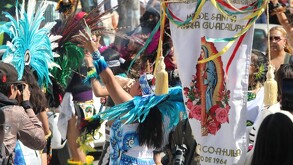 Grupo de personas caracterizadas de danza azteca junto a un estandarte de la Virgen de Guadalupe