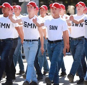 Se vea jóvenes marchando y vestidos de playera blanca y pantalón de mezclilla con cachucha.