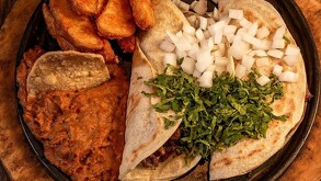 Hay un plato con tacos de carne, ceblloa, cilantro y al lado papas fritas y frijoles con totopos.