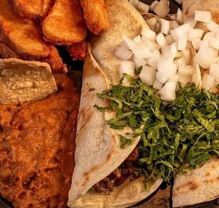 Hay un plato con tacos de carne, ceblloa, cilantro y al lado papas fritas y frijoles con totopos.