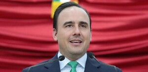 Está un hombre de traje fente a un estrado sonriendo.