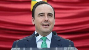 Está un hombre de traje fente a un estrado sonriendo.