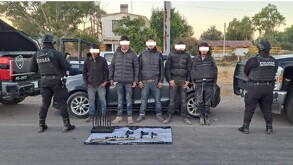 Dos policías con equipo táctico flanquean a cinco detenidos (rostros censurados) en un camino de terracería en Ojuelos. Varias armas de fuego y cartuchos