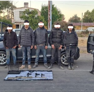 Dos policías con equipo táctico flanquean a cinco detenidos (rostros censurados) en un camino de terracería en Ojuelos. Varias armas de fuego y cartuchos