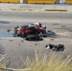 Una motocicleta roja destrozada yace en medio de una autopista, rodeada de escombros y cinta policial. Un coche oscuro con la ventanilla trasera rota
