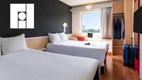 Interior de un cuarto de hotel con dos camas matrimoniales, una ventana de fondo, una televisión, maletas y ropa colgada alrededor