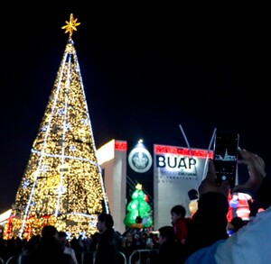 Un joven tomando una fotografía al árbol de navidad 2025 montado en el CCU de la BUAP.
