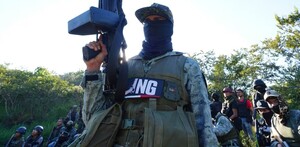 Miembros del CJNG vistiendo uniforme de camuflaje y sosteniendo armas largas sobre un terreno con plantas en Michoacán