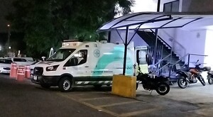 Vista lateral de una ambulancia de la Cruz Verde Las Águilas en Zapopan estacionada al exterior del hospital de noche con motos a los lados