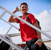 El futbolista Coccaro del Atlas se baja de un avión por las escaleras. Viste una playera roja, sonríe y hace un gesto de llamada telefónica