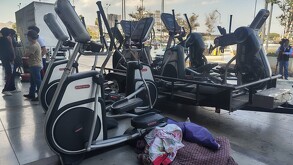 Se observan algunas máquinas de ejercicio al exterior y ropa deportiva tirada en el suelo.