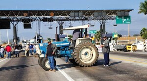 Tractor azul en medio de la carretera bloqueando casetas de Michoacán con agricultores manifestantes alrededor