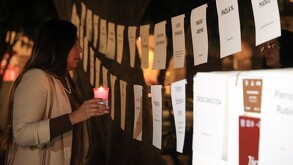 Una mujer sosteniendo una veladora con la mano, mientras lee el nombre de mujeres asesinadas en el zócalo de Puebla.