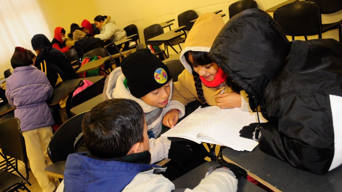 Se observan a niños con chamarras y gorros dentro de un salón de clases.