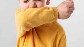 Niño con camisa en color amarillo tosiendo y cubriéndose el rostro