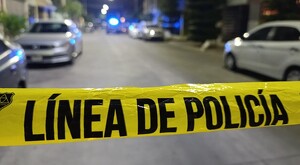 Cinta policiaca delimitando la escena del crimen con una calle y automóviles de fondo incluyendo una patrulla durante la noche