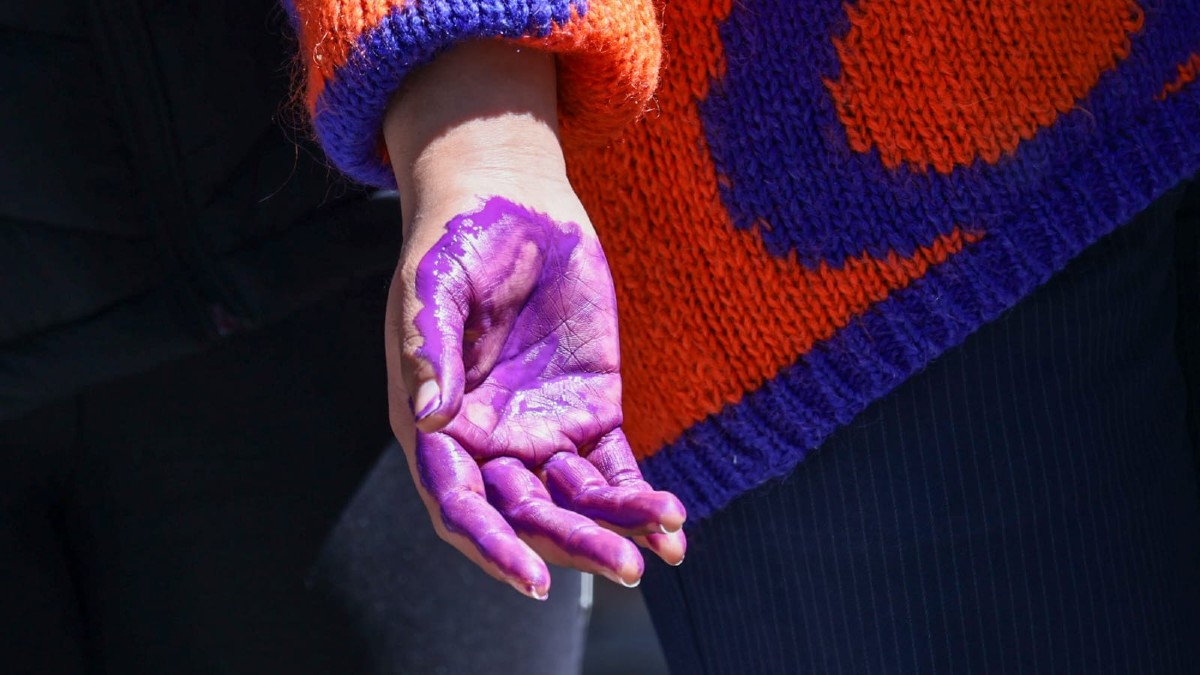 una mujer con la palma de la mano pintada de morado en relación a la violencia de género