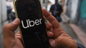 Una persona sosteniendo con las manos un celular donde se aprecian las letras de la aplicación de Uber.