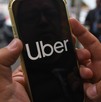 Una persona sosteniendo con las manos un celular donde se aprecian las letras de la aplicación de Uber.
