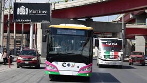 Se ven dos camiones, unas camionetas rojas y una señora a un costado.