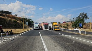 Una carretera en un día soleado, donde múltiples tráileres y camiones de carga están detenidos y bloqueando todos los carriles.