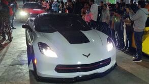 Una persona junto a un auto deportivo en un evento de arrancones clandestinos.