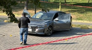 Automóvil Nissan color gris con las puertas abiertas estacionado con indicios forenses alrededor y una persona caminando frente a él y una cinta policiaca roja
